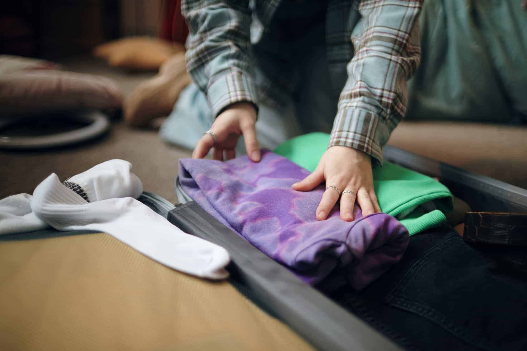 A person folds clothing into an open suitcase while packing for a stay in a treatment program.